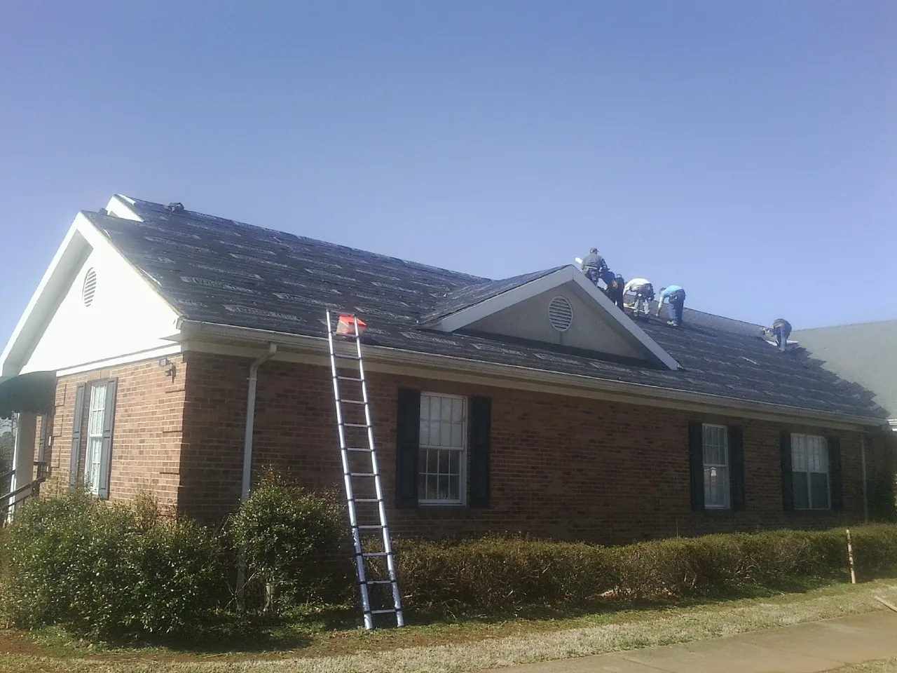 Crew tearing shingles off a brick ranch roof with a ladder set — Emergency Roof Repair work by our crew in Newburgh