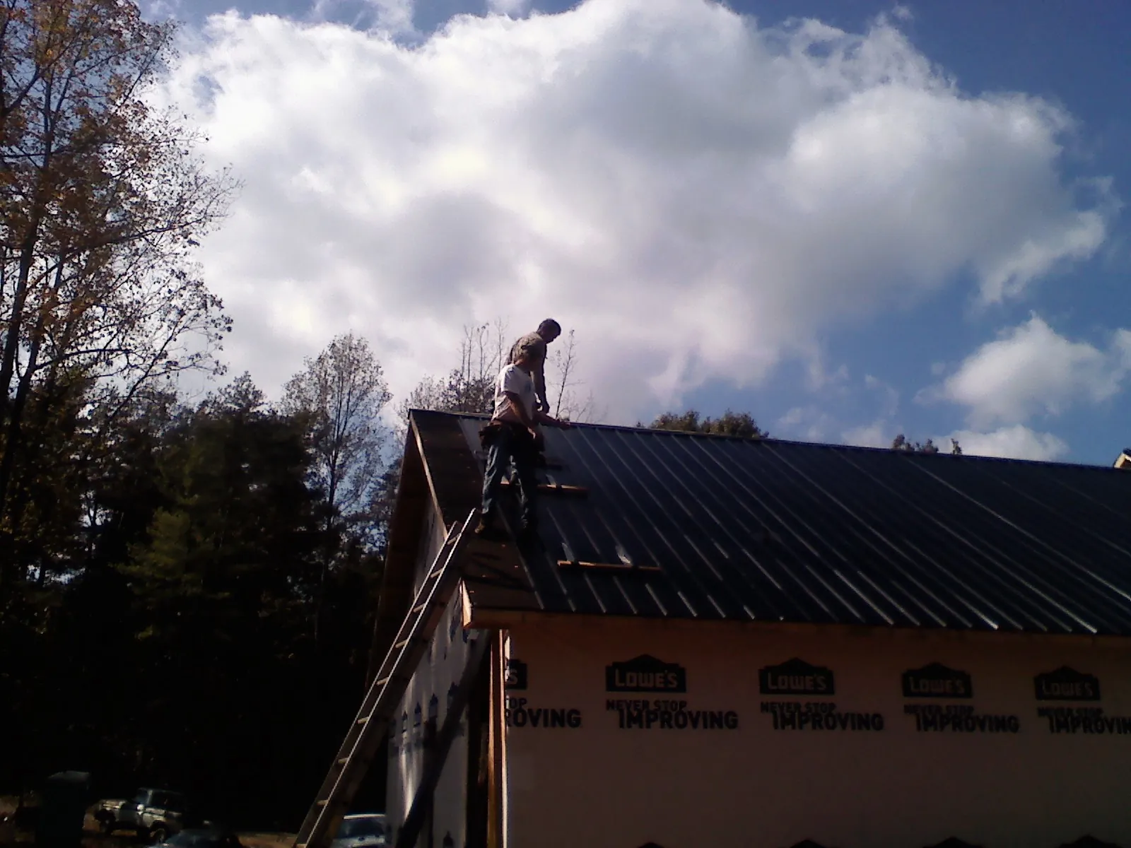 Roofer fastening dark metal panels high against a cloudy sky, from a Roof Inspection job in Newburgh