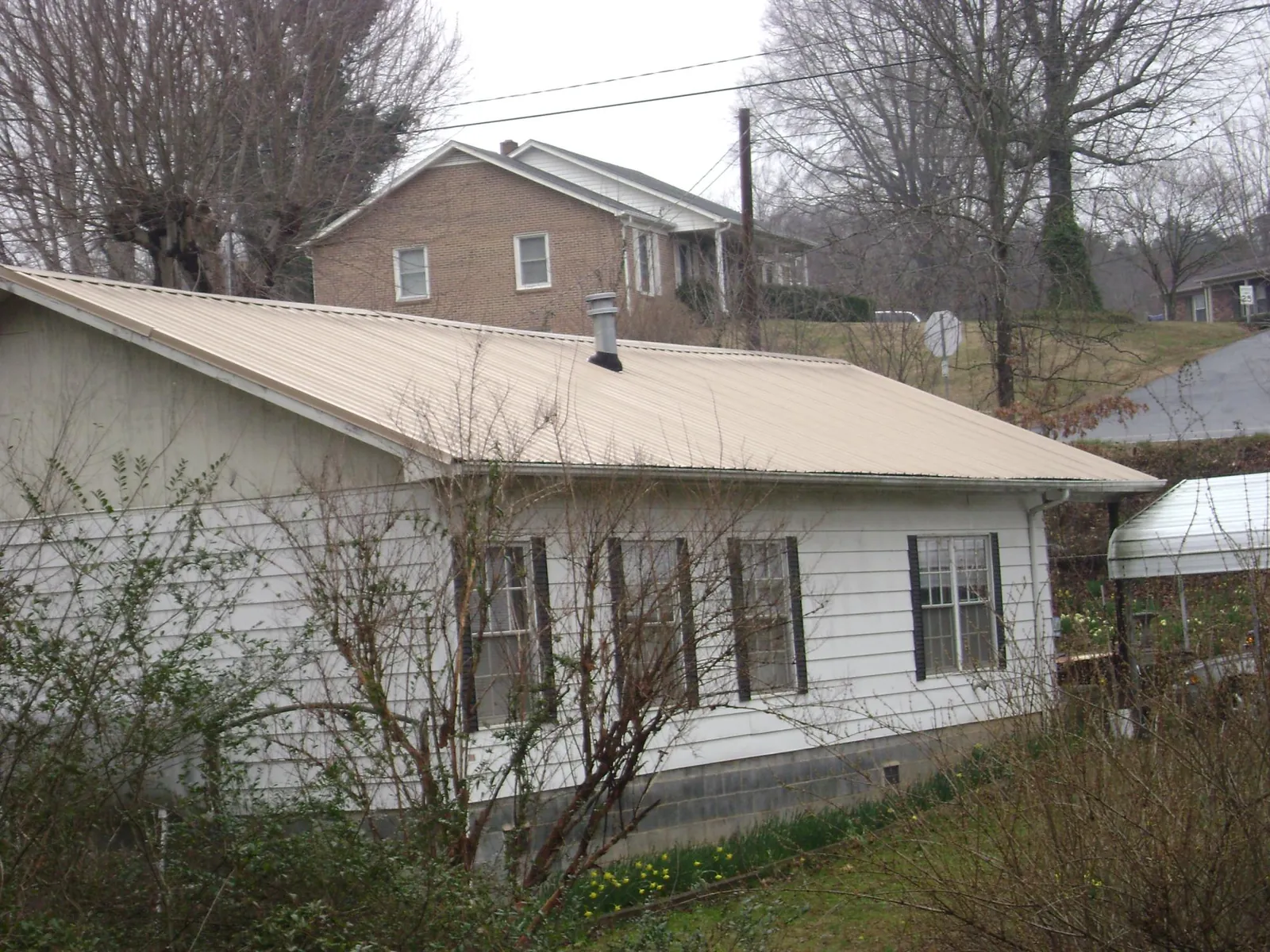 Tan metal roof on a white sided house set into a hillside — Commercial Roofing by Roofing Brothers in Newburgh